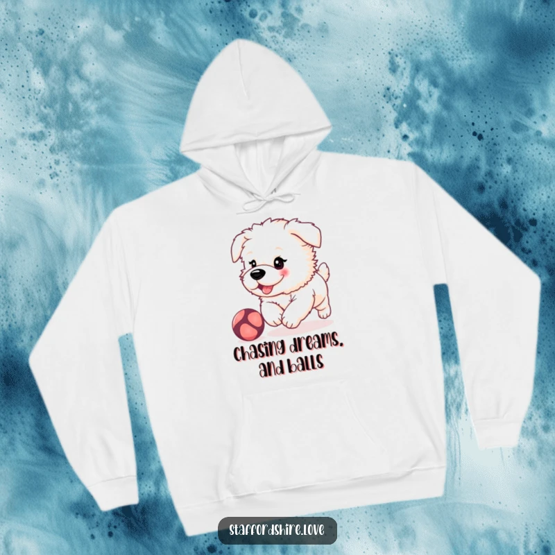 Funny, fluffy Staffordshire puppy with rosy cheeks, playfully chasing a bouncing ball on a warm and cozy hoodie.